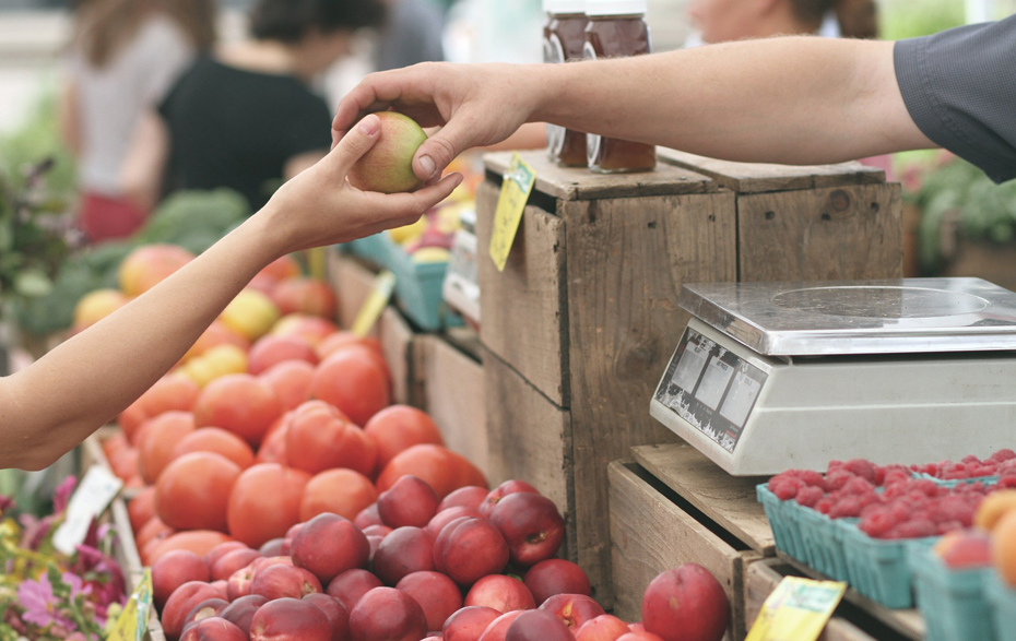 Foto: Eine Hand übergibt einen Apfel in die Kundenhand über den Marktstand hinweg. Foto: Eine Hand übergibt einen Apfel in die Kundenhand über den Marktstand hinweg.