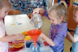 Foto: Mädchen füllt Wasser in eine Flasche mit einem Trichter.