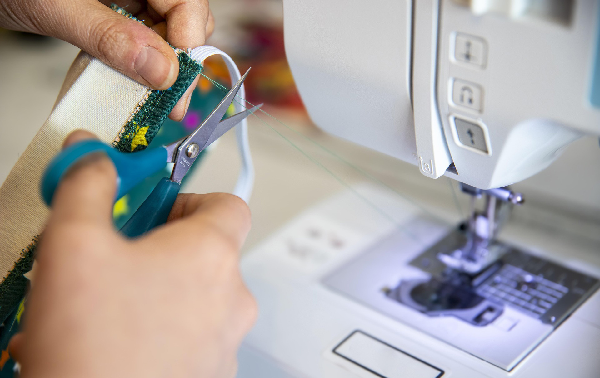 Foto: Hand mit Schere beim Schneiden vor einer Nähmaschine Foto: Hand mit Schere beim Schneiden vor einer Nähmaschine