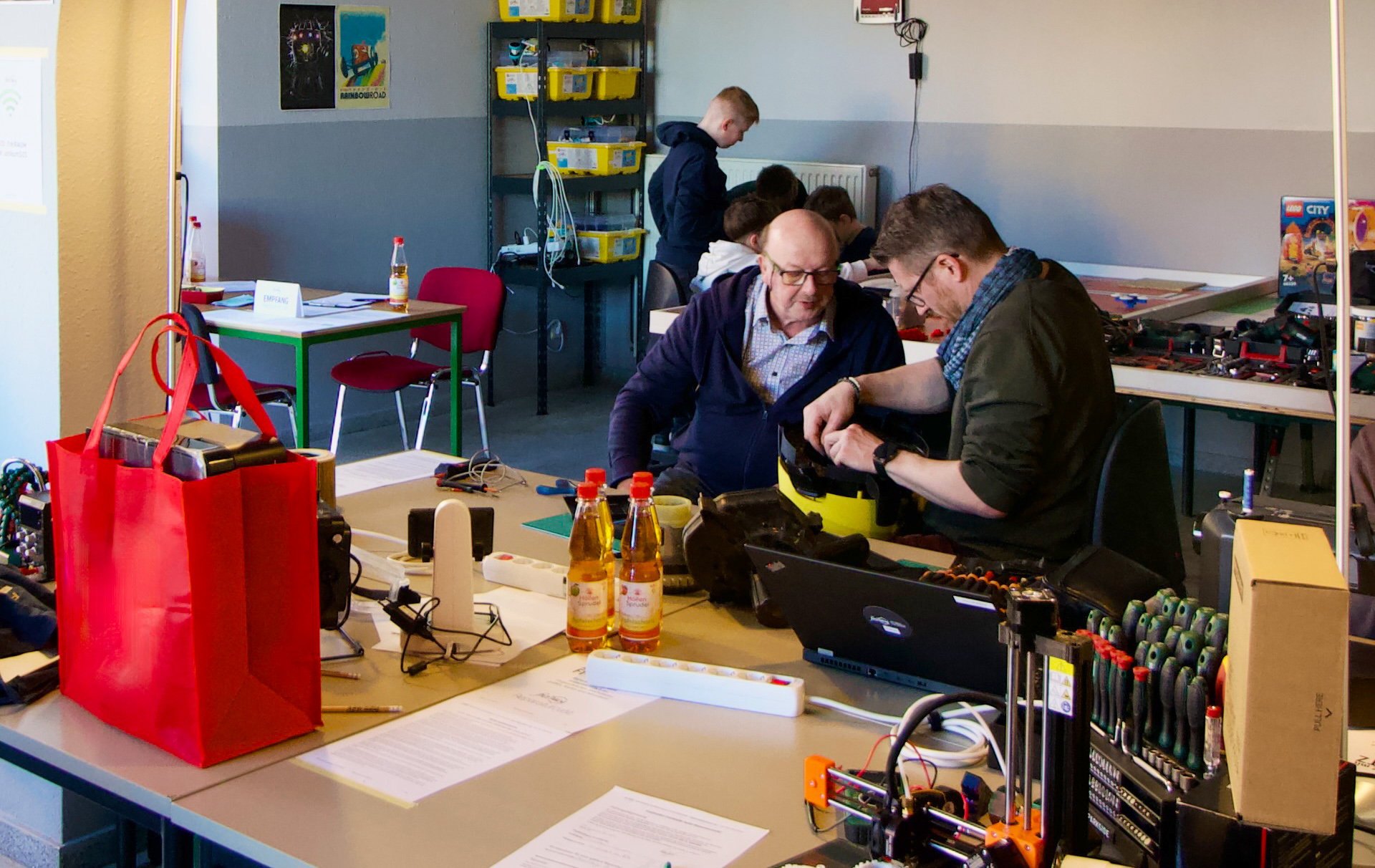 Foto: Blick in die Werkstatt mit 3 Personen beim Reparieren Foto: Blick in die Werkstatt mit 3 Personen beim Reparieren