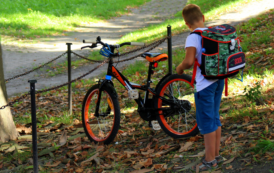 Foto: Junge mit Schulranzen neben einem Fahrrad im Park Foto: Junge mit Schulranzen neben einem Fahrrad im Park