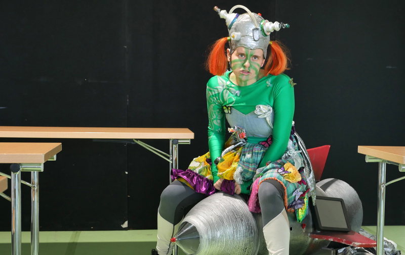 Foto: dSchauspielerin als Außerirdische verkleidet sitzt auf einer Rakete im Klassenzimmer Foto: dSchauspielerin als Außerirdische verkleidet sitzt auf einer Rakete im Klassenzimmer